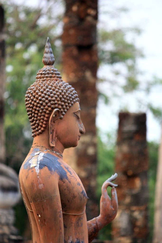 Side view of a weathered Buddha sculpture in a historic Asian temple setting.